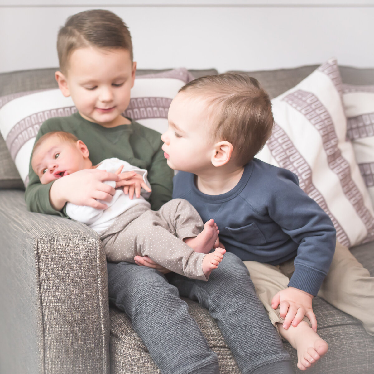 big brothers holding their new baby brother sitting on the sofa