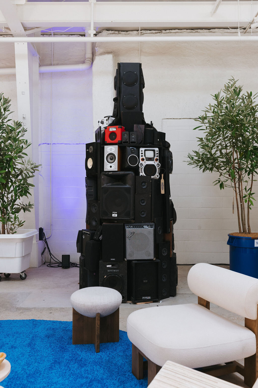 Installation of stacked black speakers with lounge seating and plants.