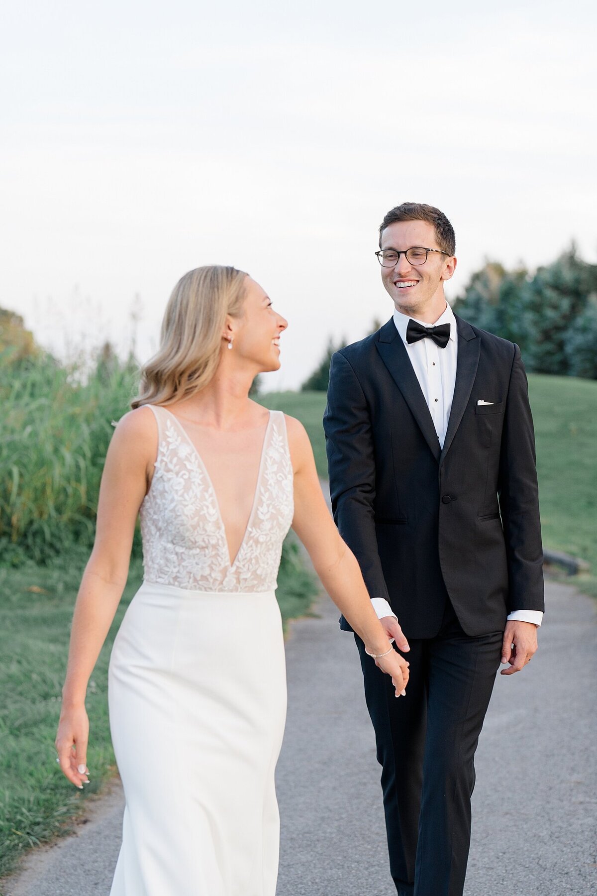 bride and groom hold hands and laugh together as they walk on a path on the Pinnacle gold club course for their wedding