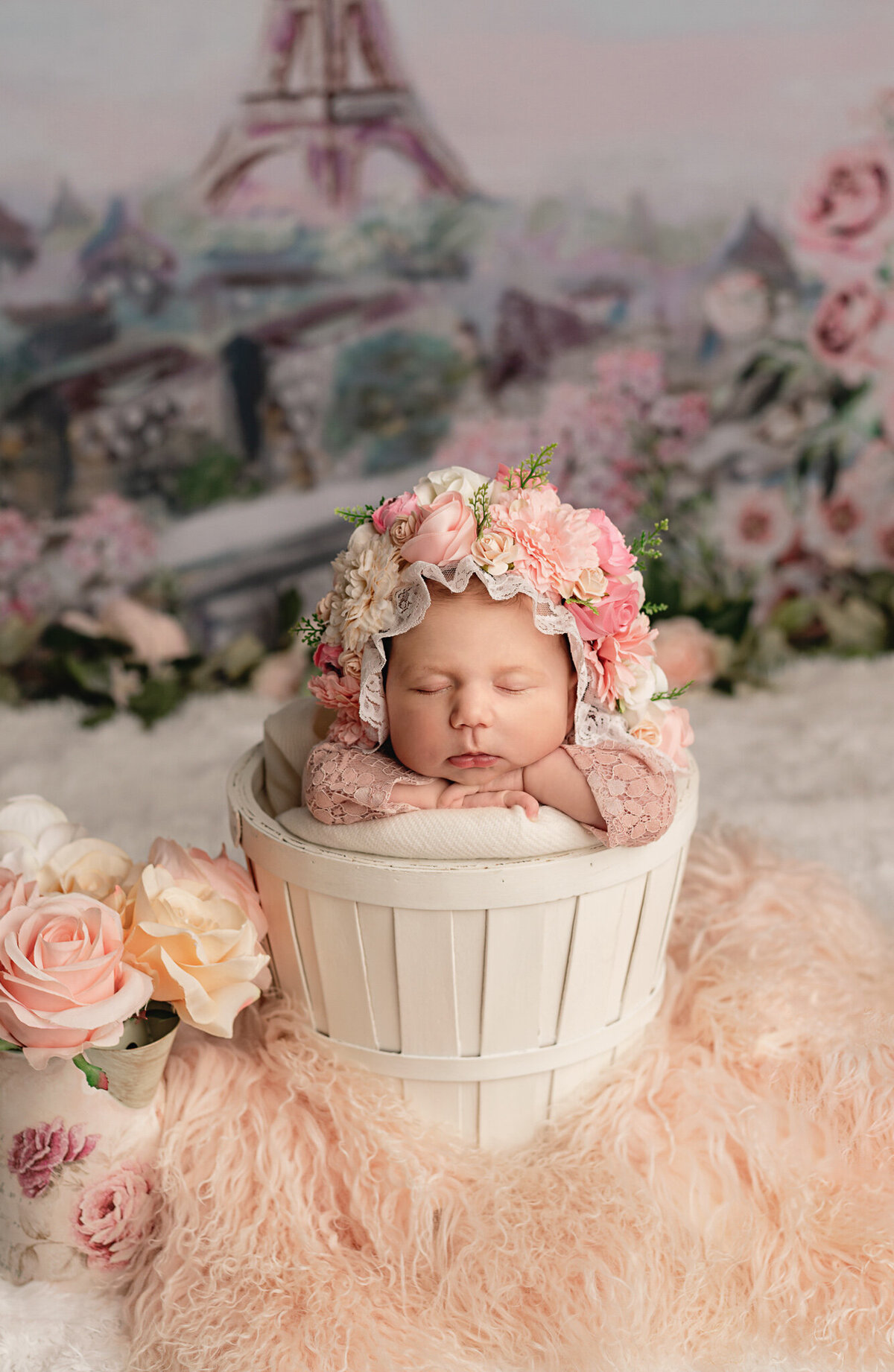 Newborn Photo of baby in a white bucket wearing a floral bonnet with Paris theme setup, studio in Greater Toronto area.