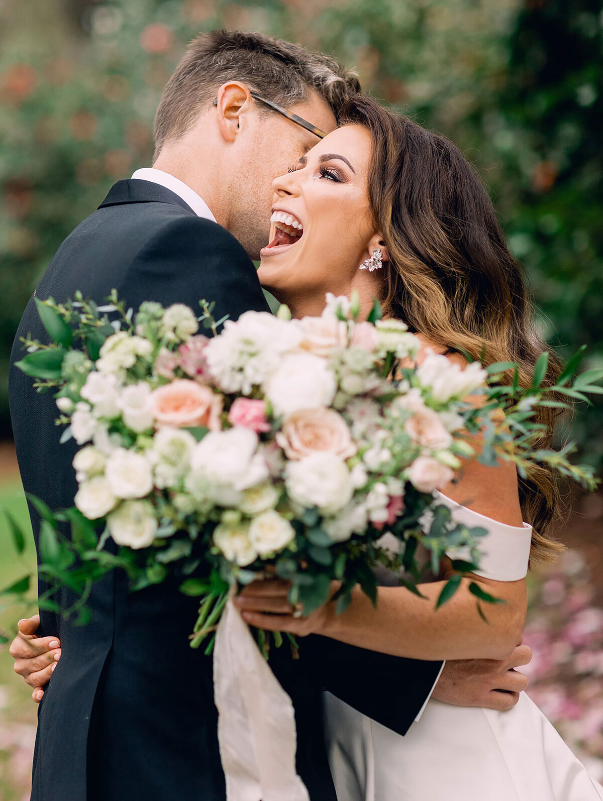 Groom embraces his stunning bride while she holds wedding bouquet