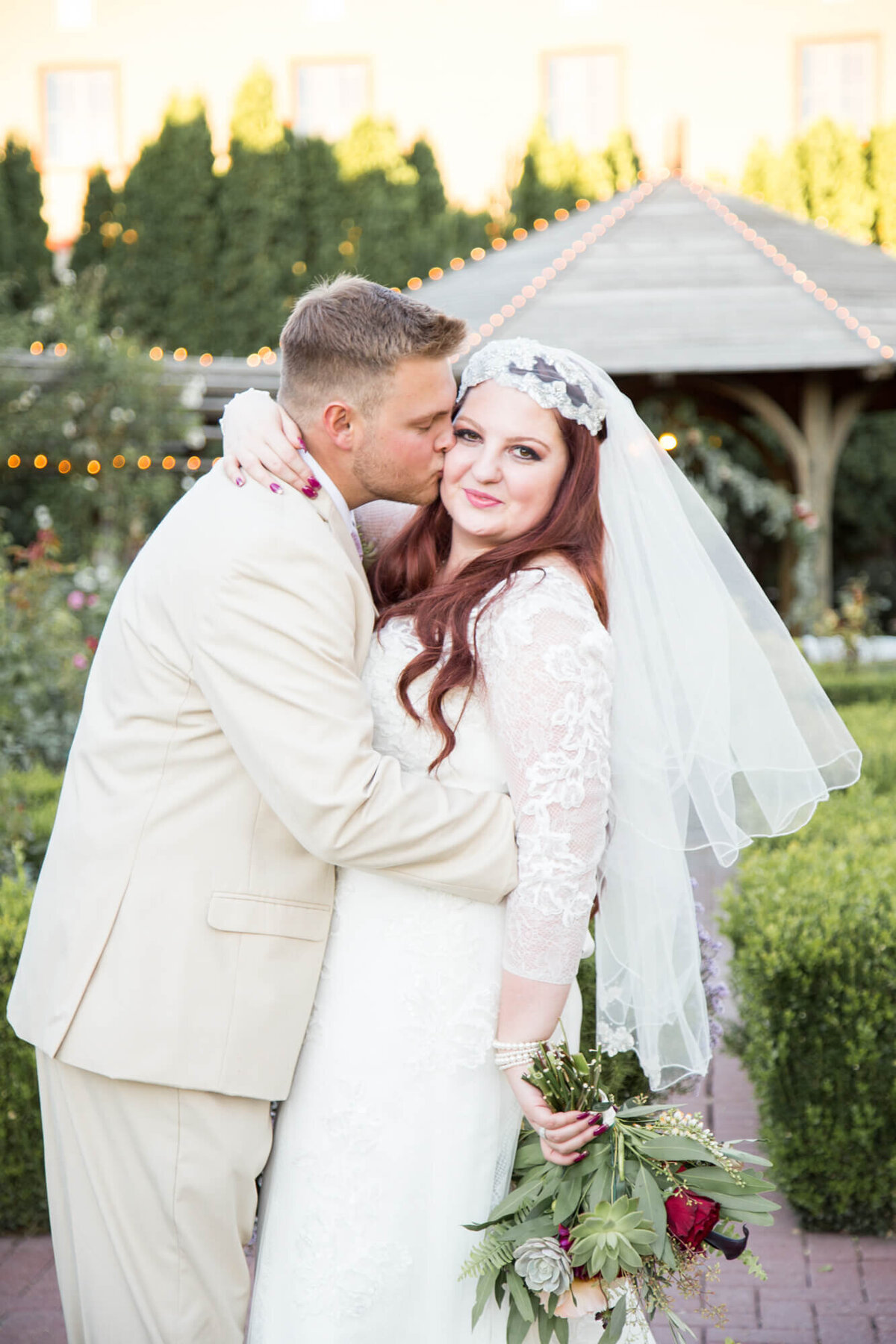 groom kissing bride in a rose garden