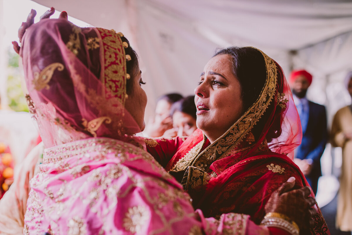 A mother sheds a tear as she hugs the bride goodbye after the sikh wedding