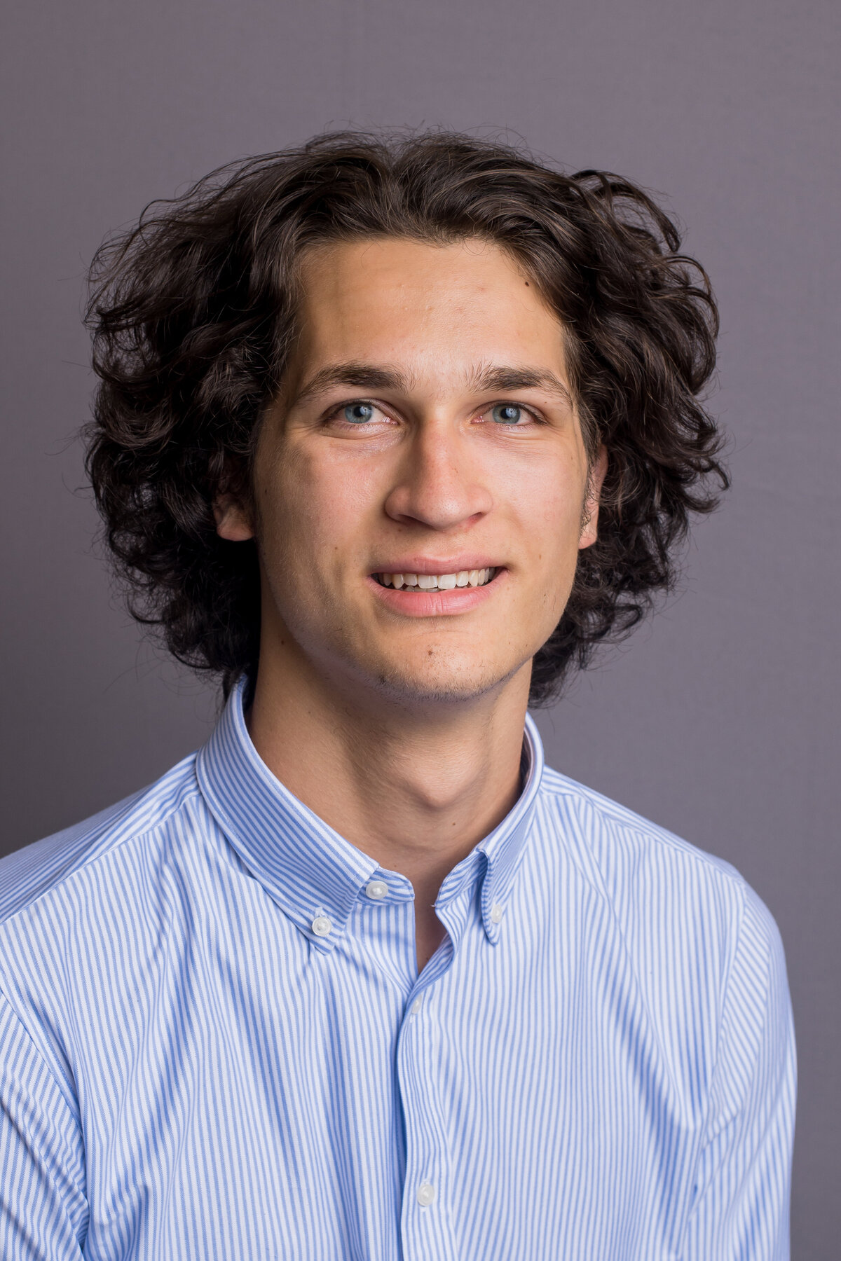 a man with dark curly hair poses in a blue shirt