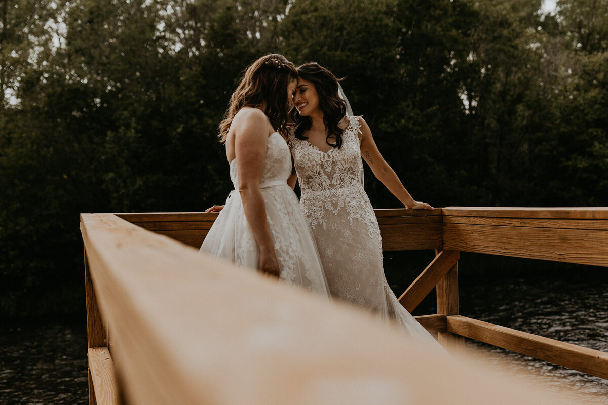 two brides standing on a dock together over a river
