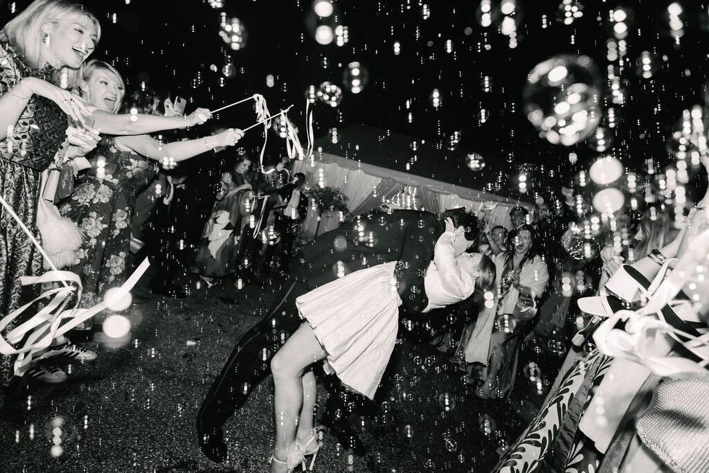 Bride and groom share a dramatic dip kiss during their bubble exit, captured in black and white outside their Highlands, NC wedding reception.