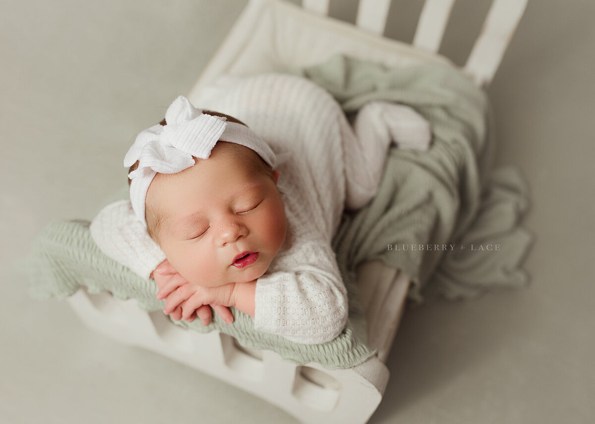 newborn baby girl posed on bed sleeping wearing green and white