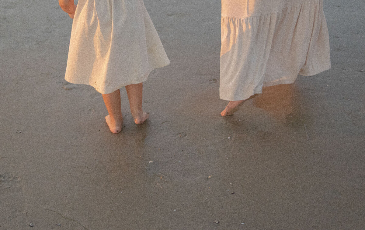 Close-up of mother and child’s feet on the sandy shore
