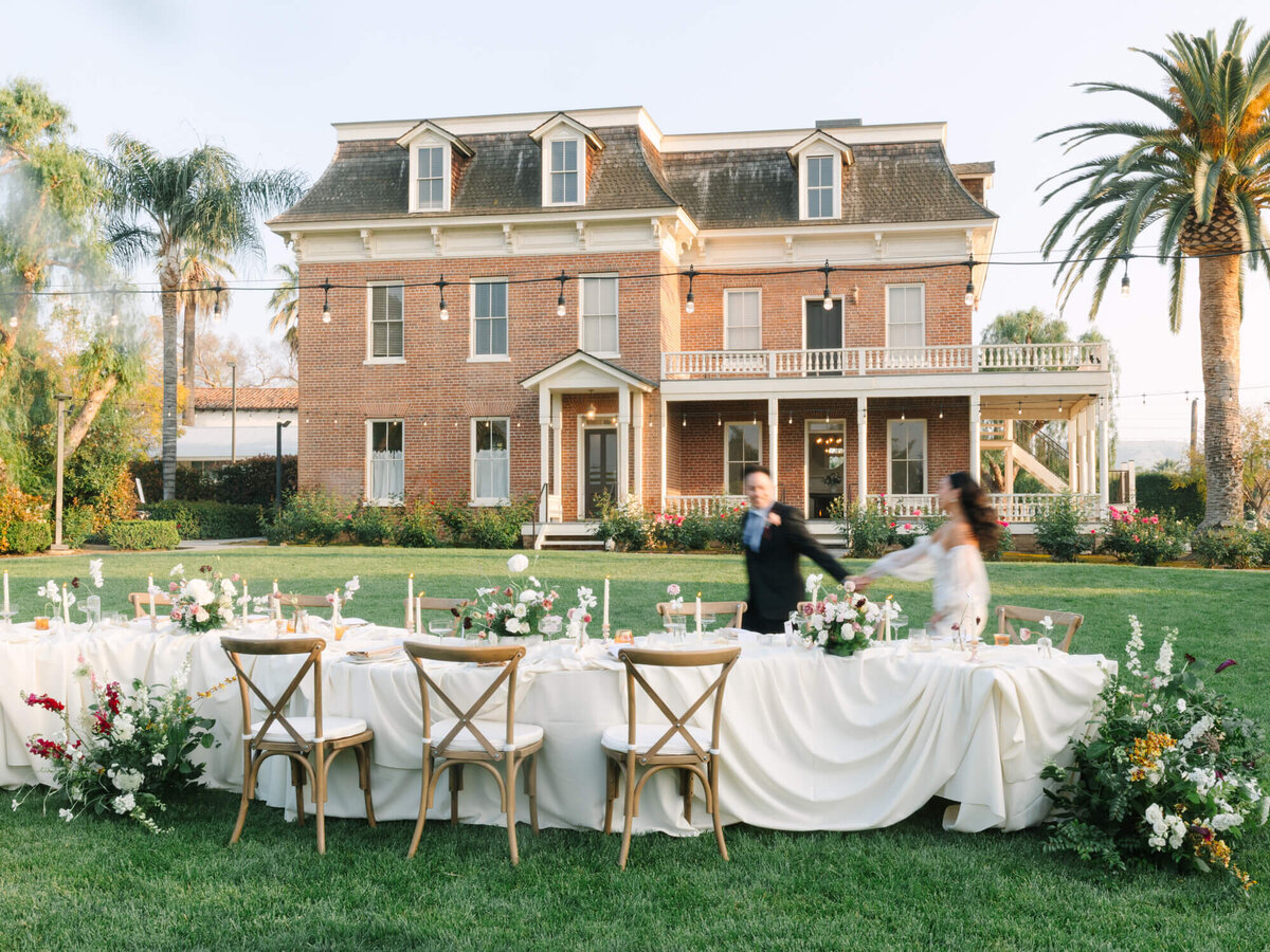 A charming outdoor wedding setup features a long table with white linens and floral arrangements on a lawn.