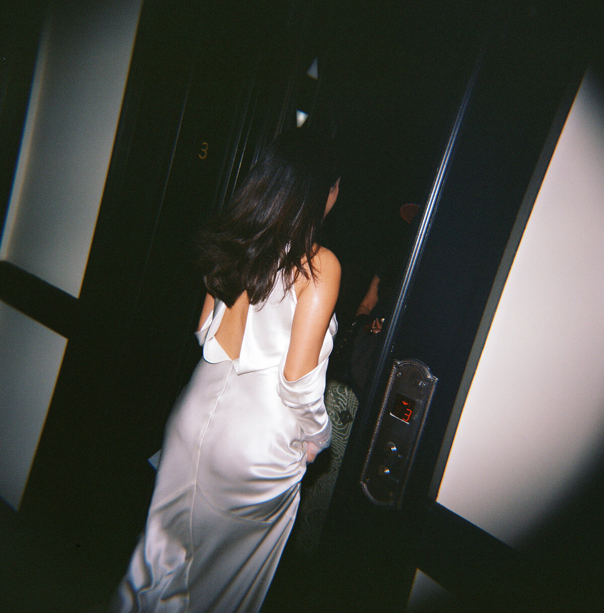Flash film photo of a bride in a satin backless gown walking into an elevator during her New York City elopement. 