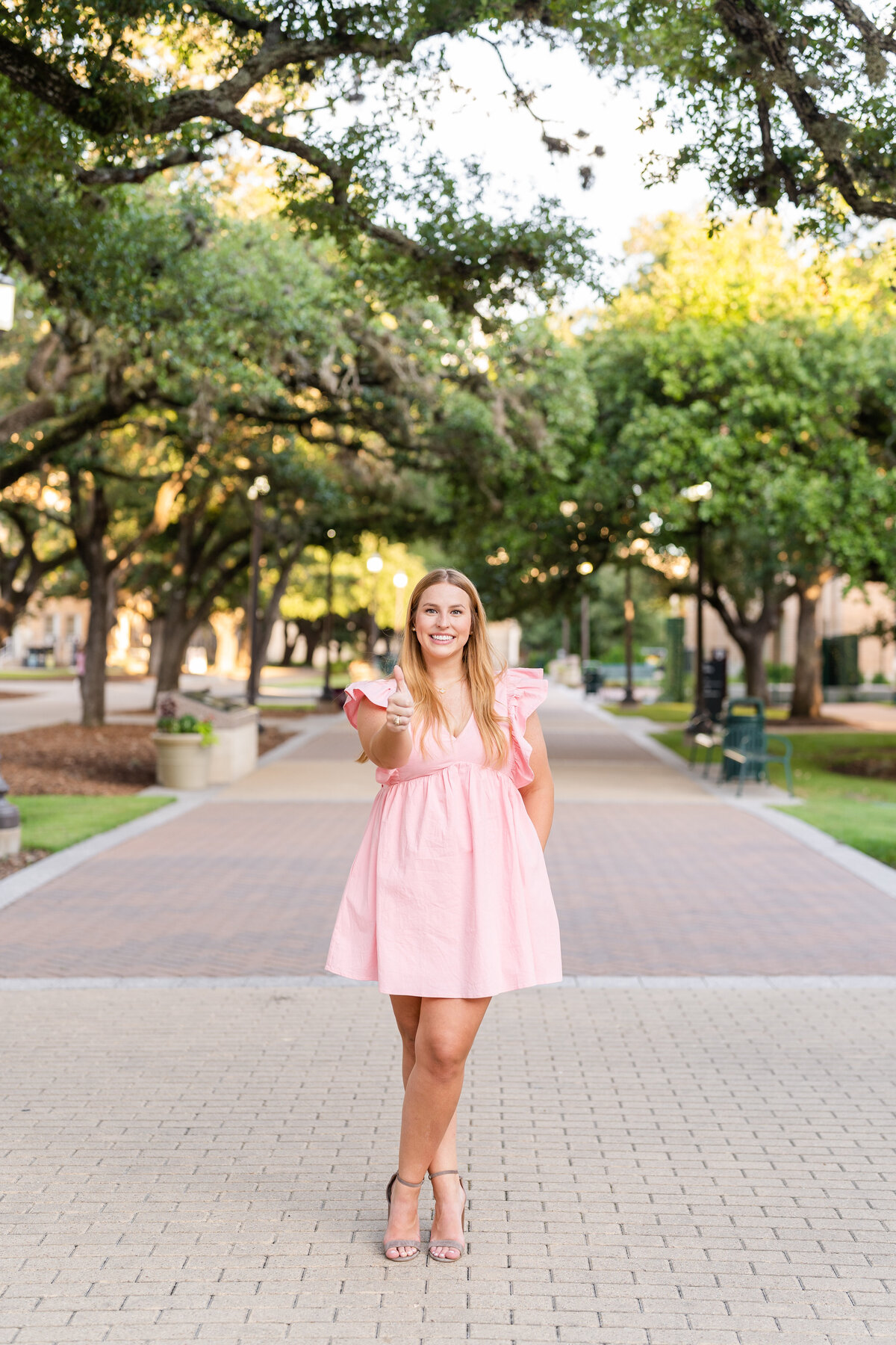 Texas A&M senior girl wearing a pink dress and hand in pocket with thumbs up in Military Plaza