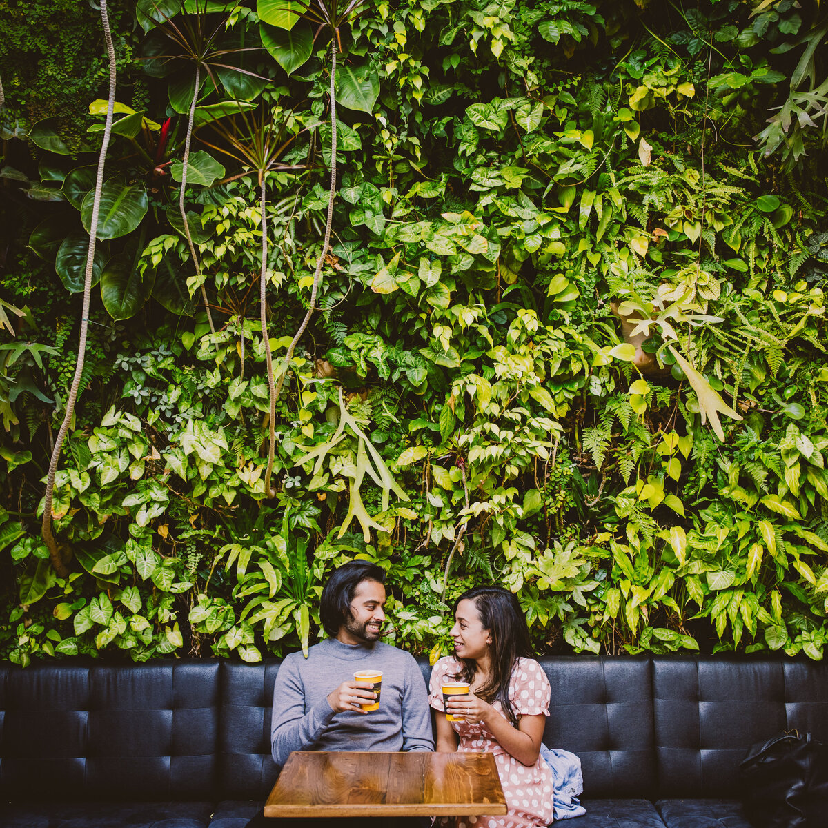 An engaged couple sitting inside devocion cafe having coffee in front of a green wall in brooklyn