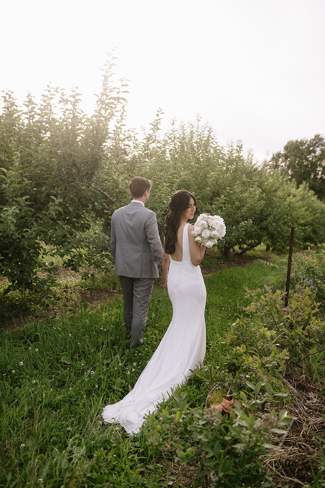 A bride shows off a large white bouquet in the orchard of Verger du Flanc Nord.