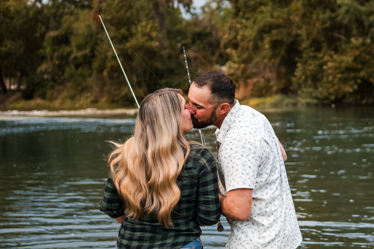 Engaged couple splashing water toward the camera while laughing in the Guadalupe River during lifestyle engagement session in New Braunfels, Texas.