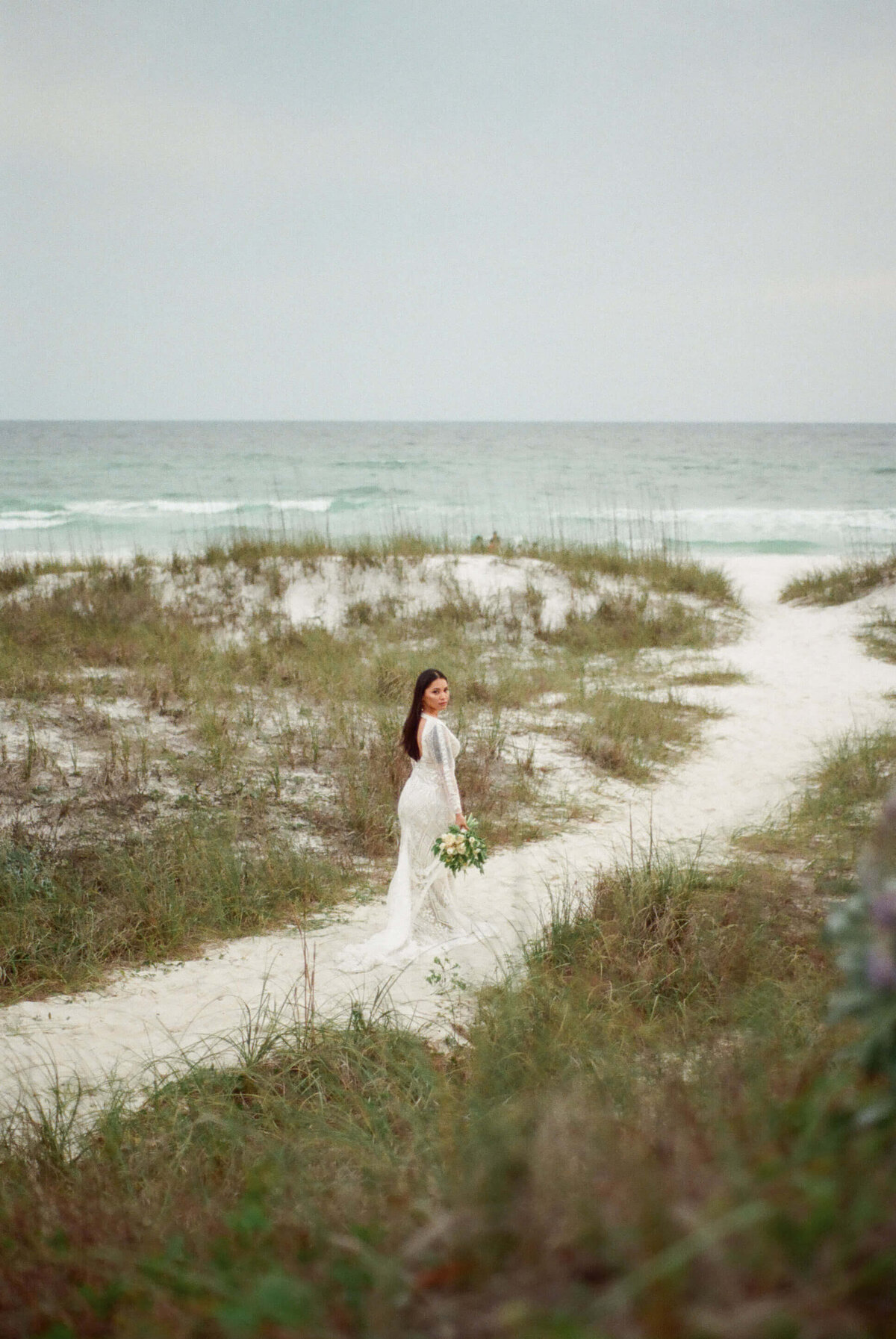 asian bride in bridal dress and veil walks on beach path - taken by panama city fl photographer Brittney Stanley