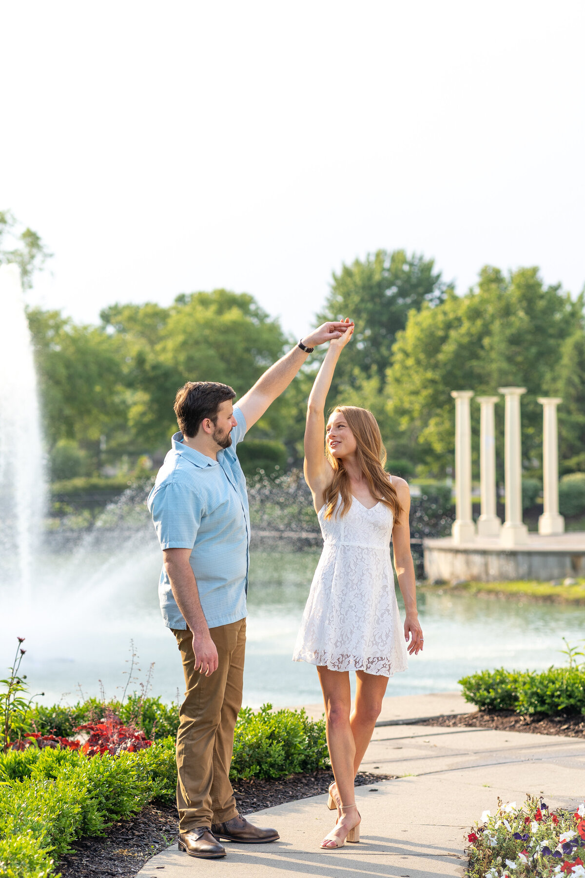 male and female twirling along a curved path surrounded by floral landscaping with water fountain in background
