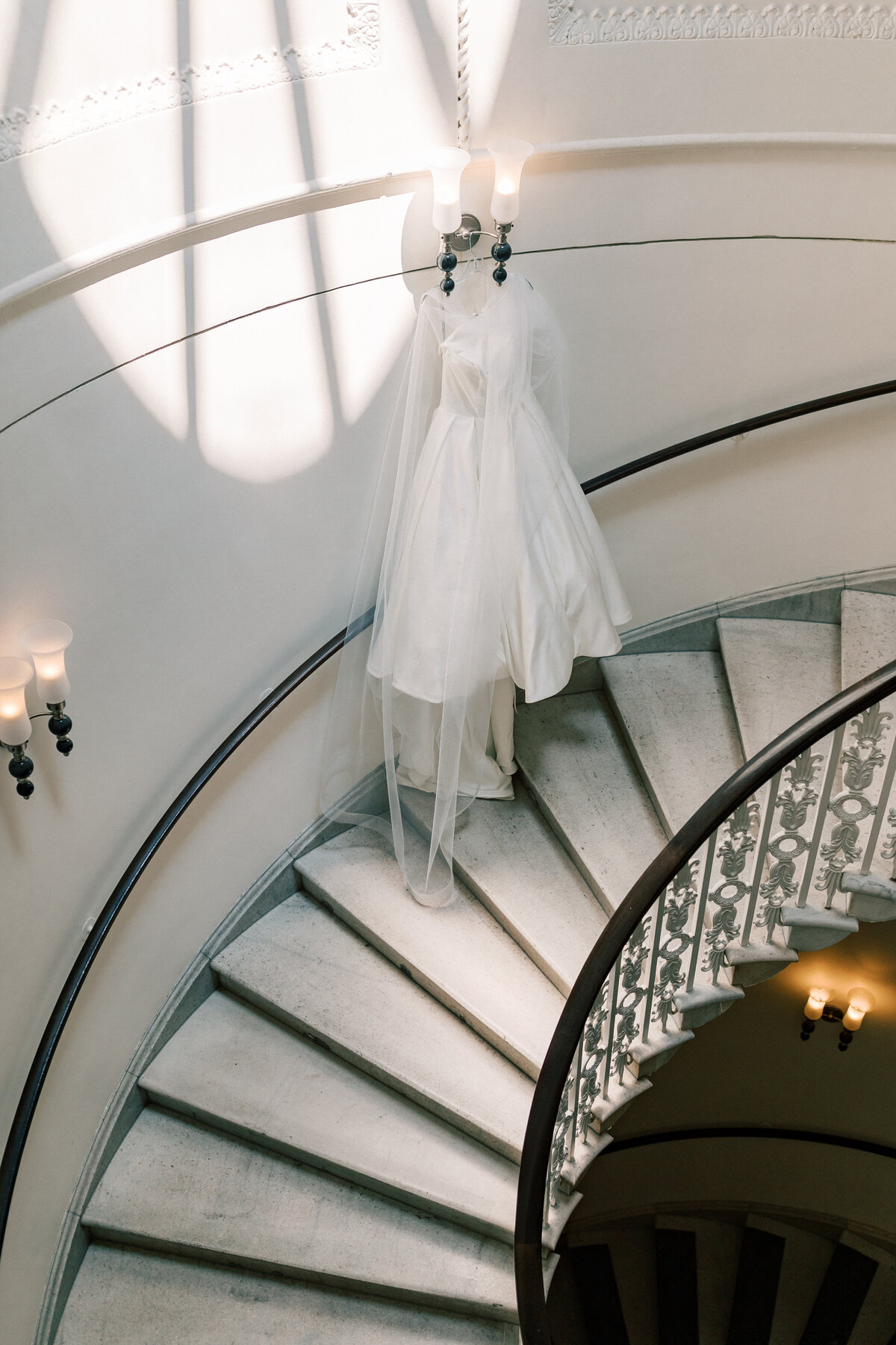 Satin wedding dress hanging on sweeping staircase inside Hotel Monaco Washington DC.