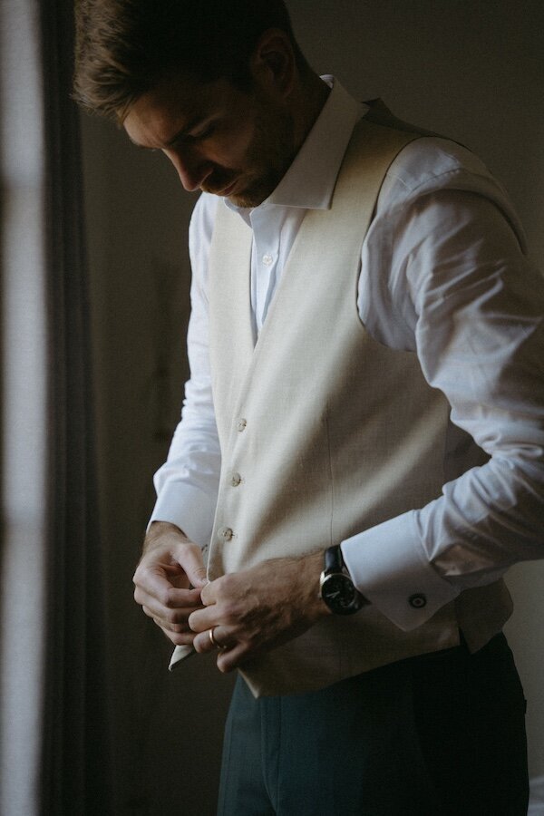 Le marié ajuste son gilet crème avant la cérémonie, concentré et élégant dans la lumière naturelle. Par Kamescop, photographe de mariage.