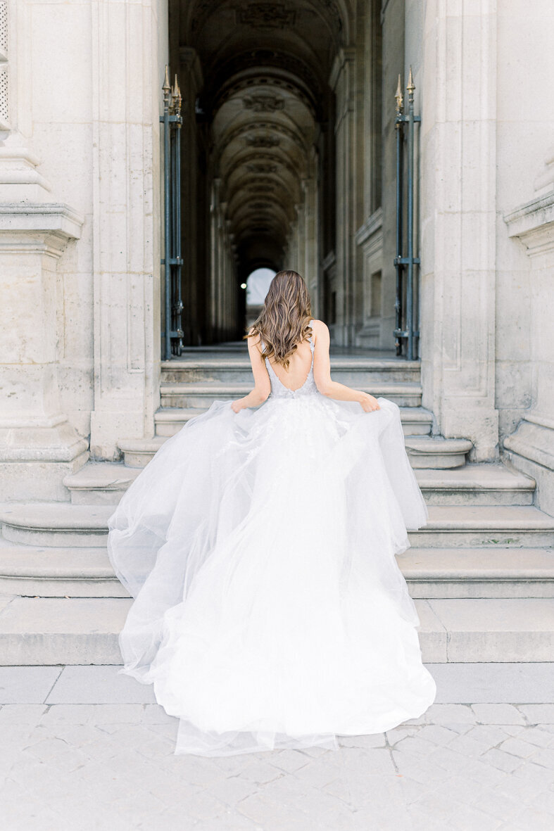 Erlebe zeitlose Schönheit und Eleganz in diesem romantischen Brautporträt, aufgenommen auf den majestätischen Stufen des Louvre. Die zarte Anmut der Braut und die Pracht ihrer weißen Rosen verleihen diesem Moment eine unvergessliche Aura. Lass dich von der Atmosphäre der Liebe und Raffinesse verzaubern. Fine Art Hochzeitsfotografie von Alla Regier Photographie.