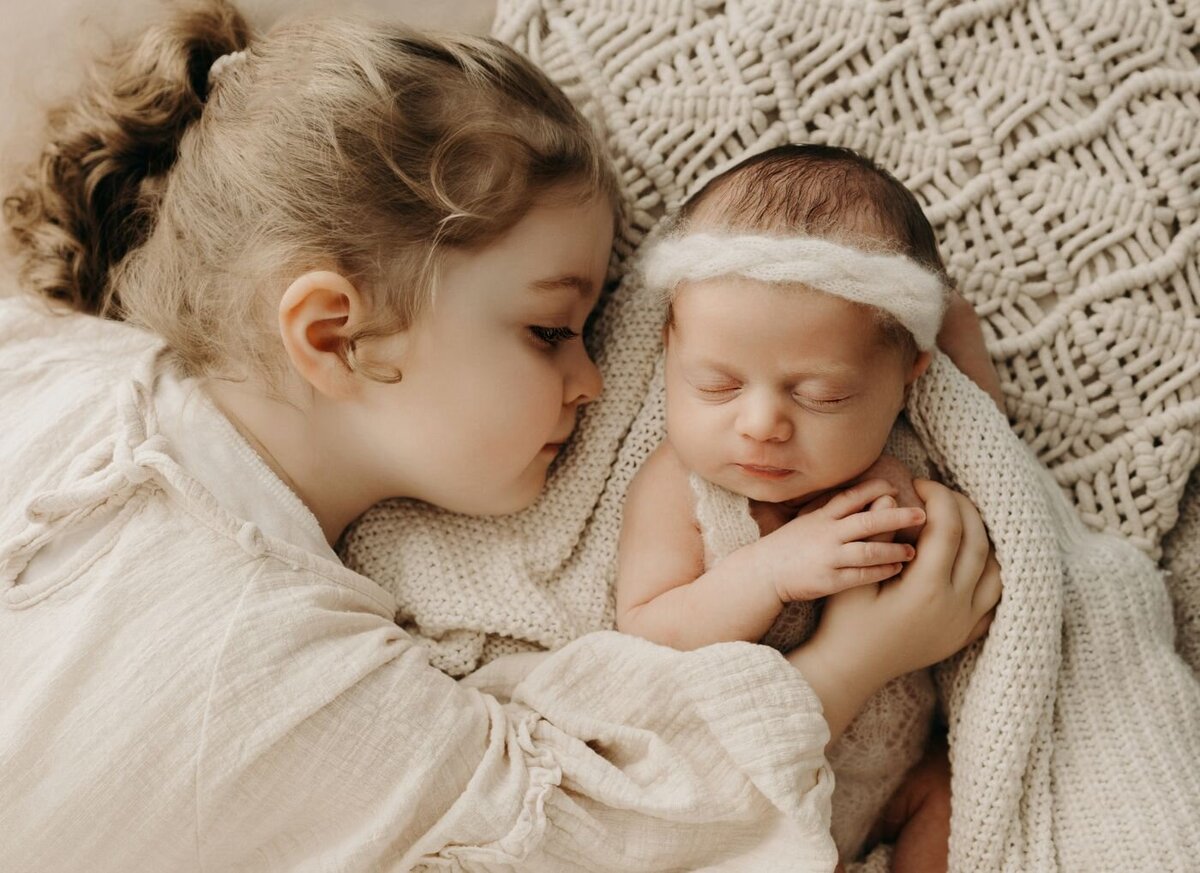 Sweet moment between siblings: older sister gently looking at her sleeping newborn baby brother during a Mullingar family photoshoot