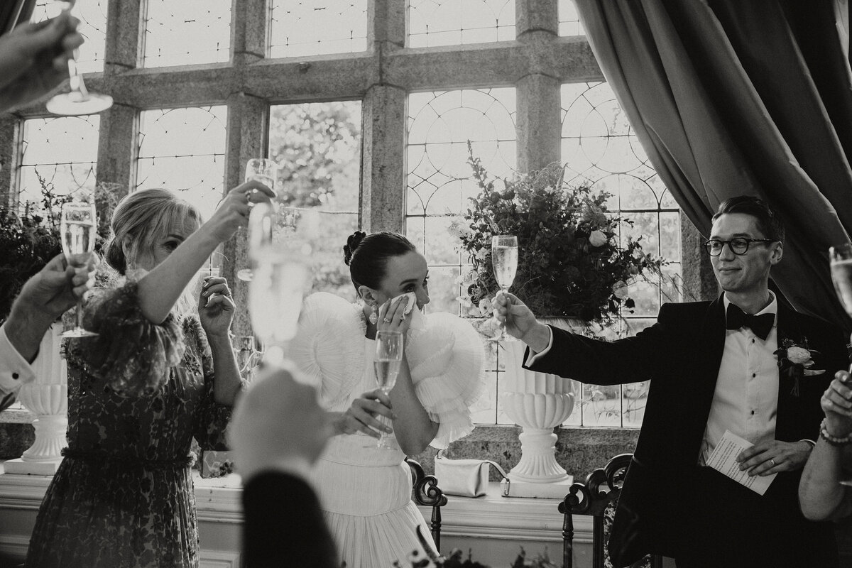 Balck and white image of bridal party raising glasses during the speeches