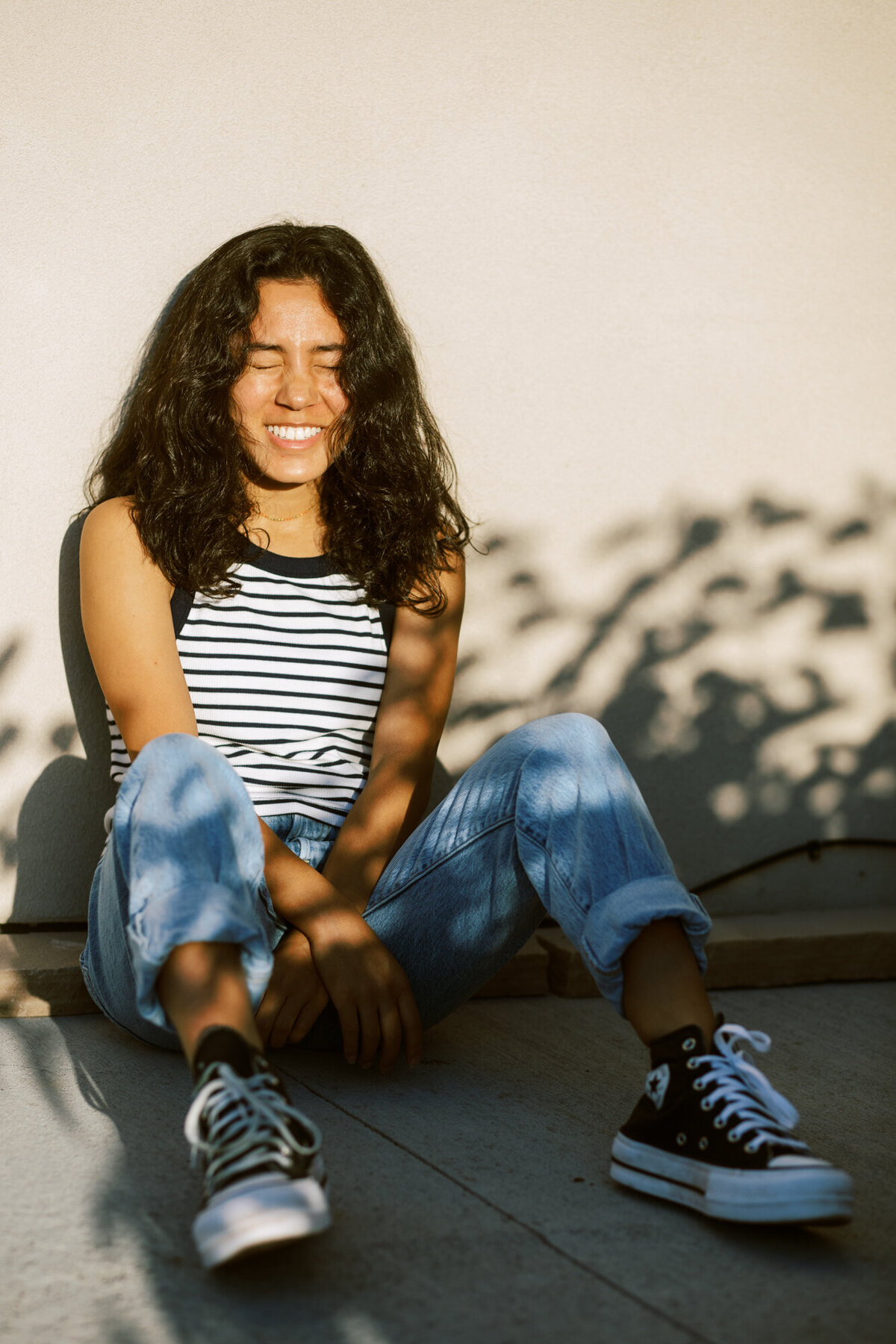 girl in tank and sneakers sits against a wall