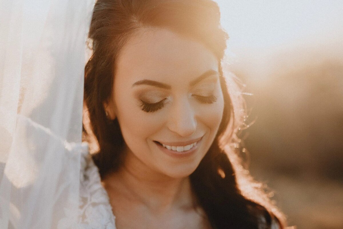 A close-up of a smiling bride with her veil softly diffusing the sunlight, capturing the glow and happiness of a wedding day.