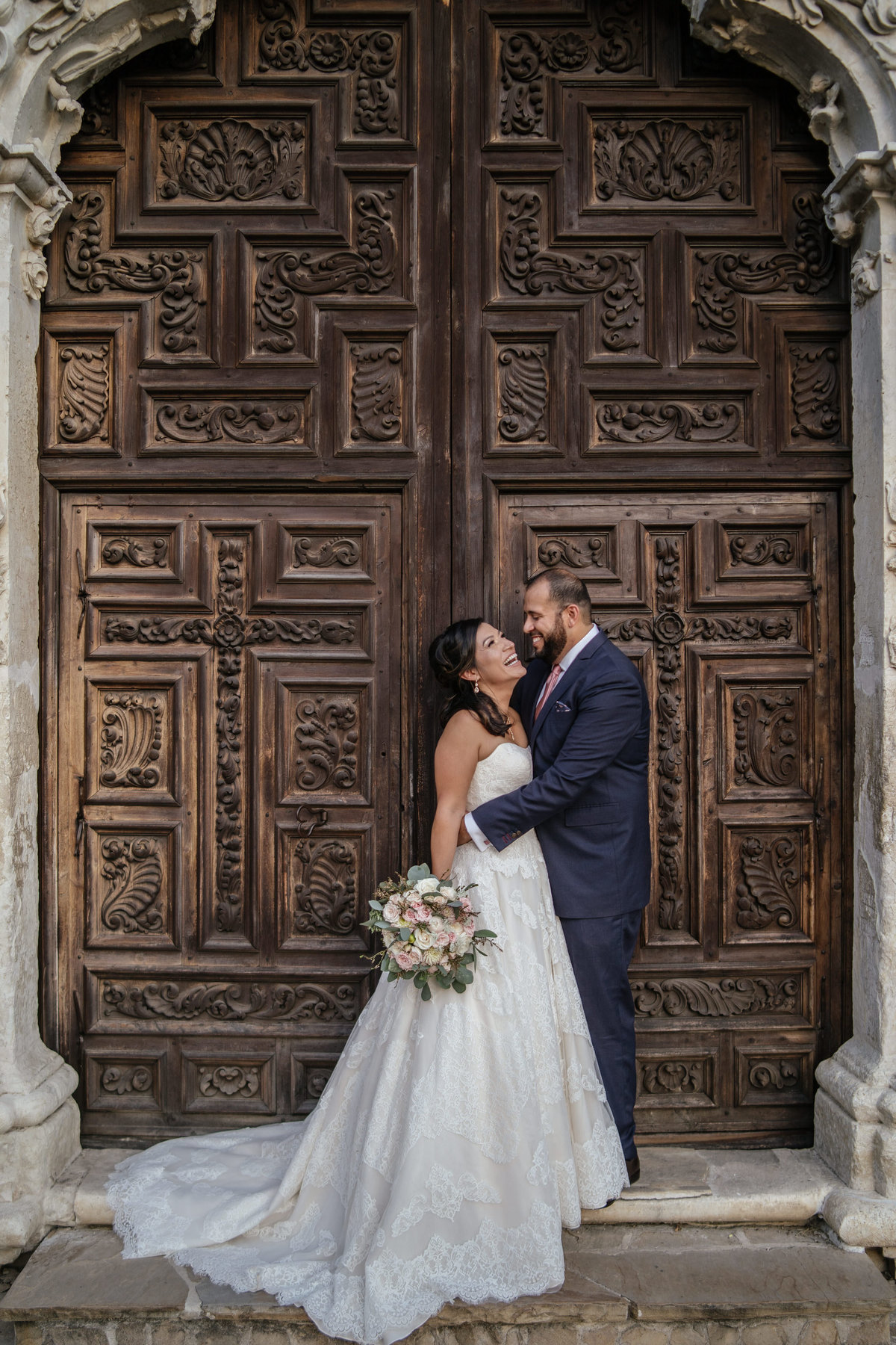 Bride and groom holding each other in front of the door at Mission San Jose in San Antonio