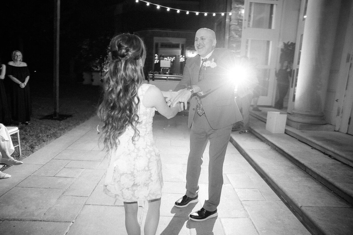Bride and father share a first dance under the lights of the mansion as the sun sets.