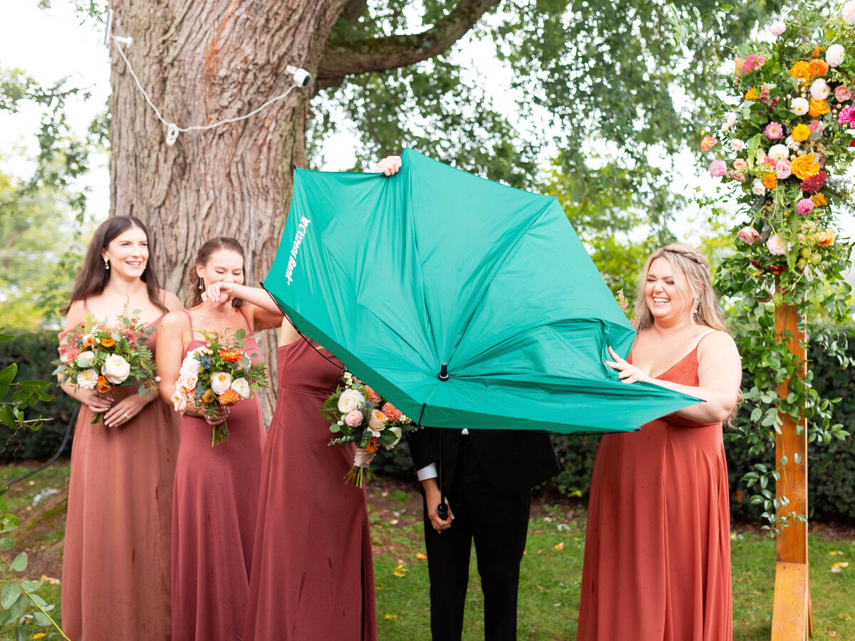 Bridesmaids laugh as an umbrella malfunctions.