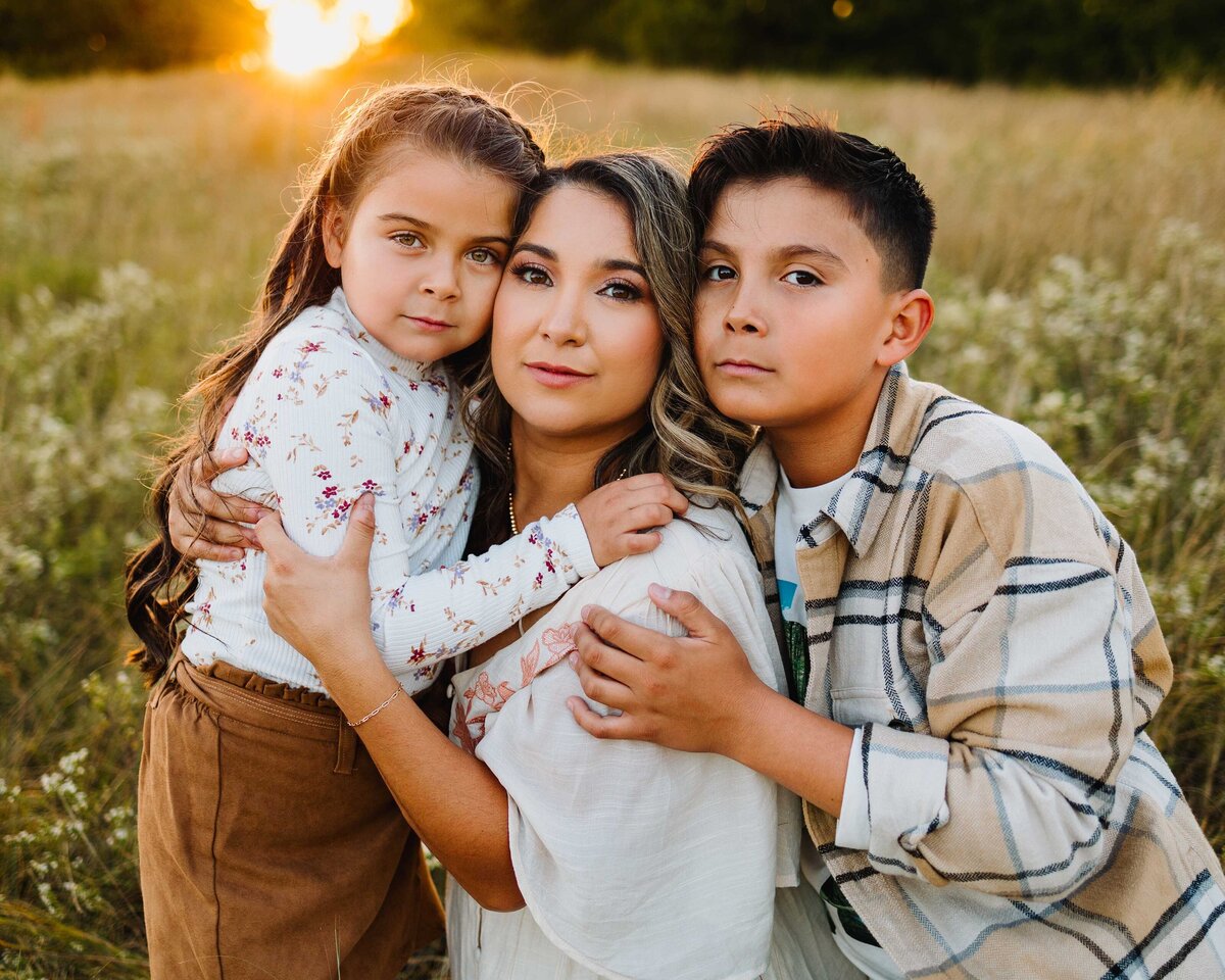 The Albuquerque family photography expert captures a heartwarming moment of a mother embracing her two children. The mother, dressed in a floral coat and brown pants, hugs her daughter tenderly, while her son affectionately embraces her.