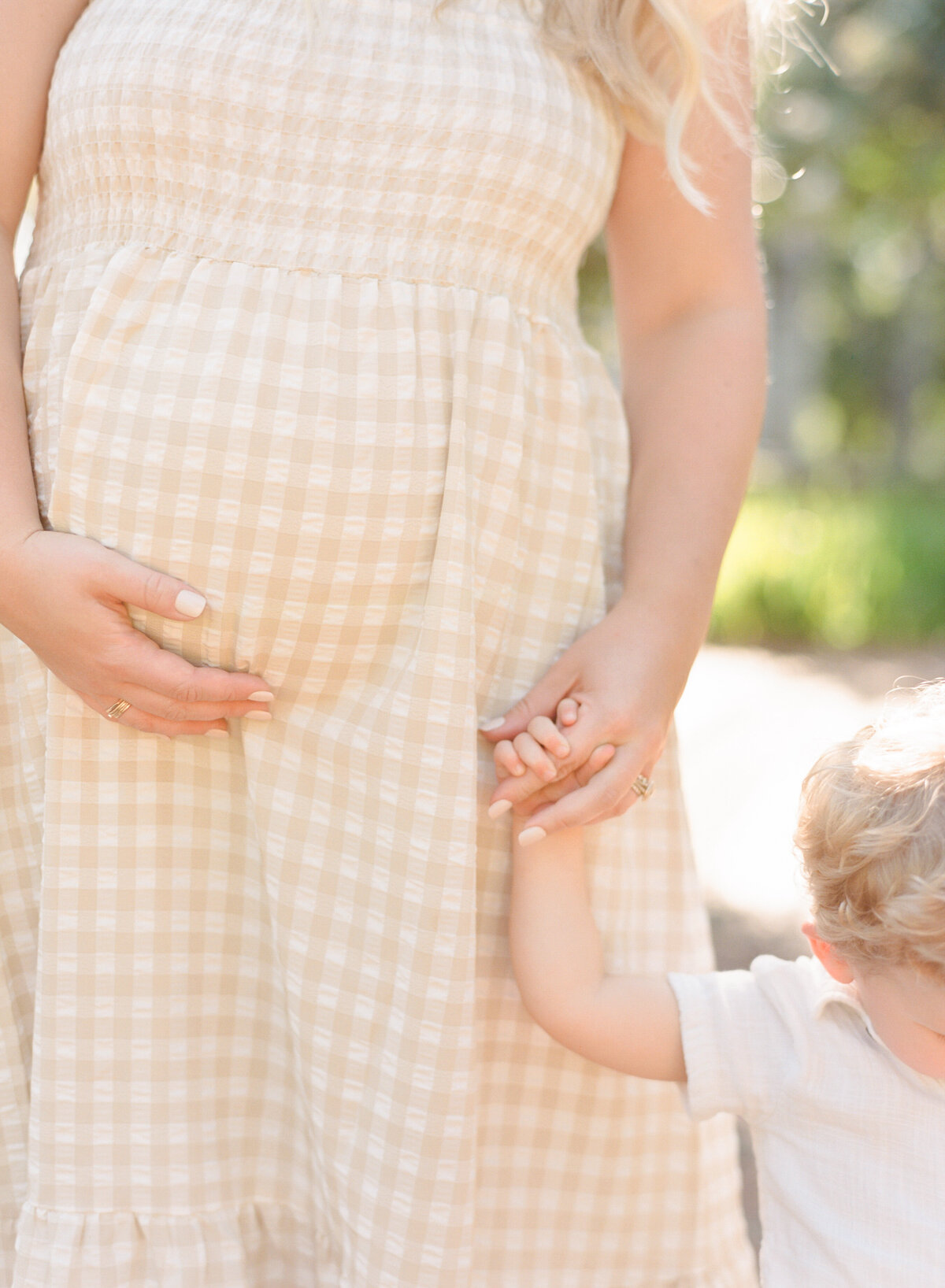 Mom holds toddler's hand and cradles her belly during her maternity session in Wake Forest. Image by Raleigh maternity photographer A.J. Dunlap Photography.