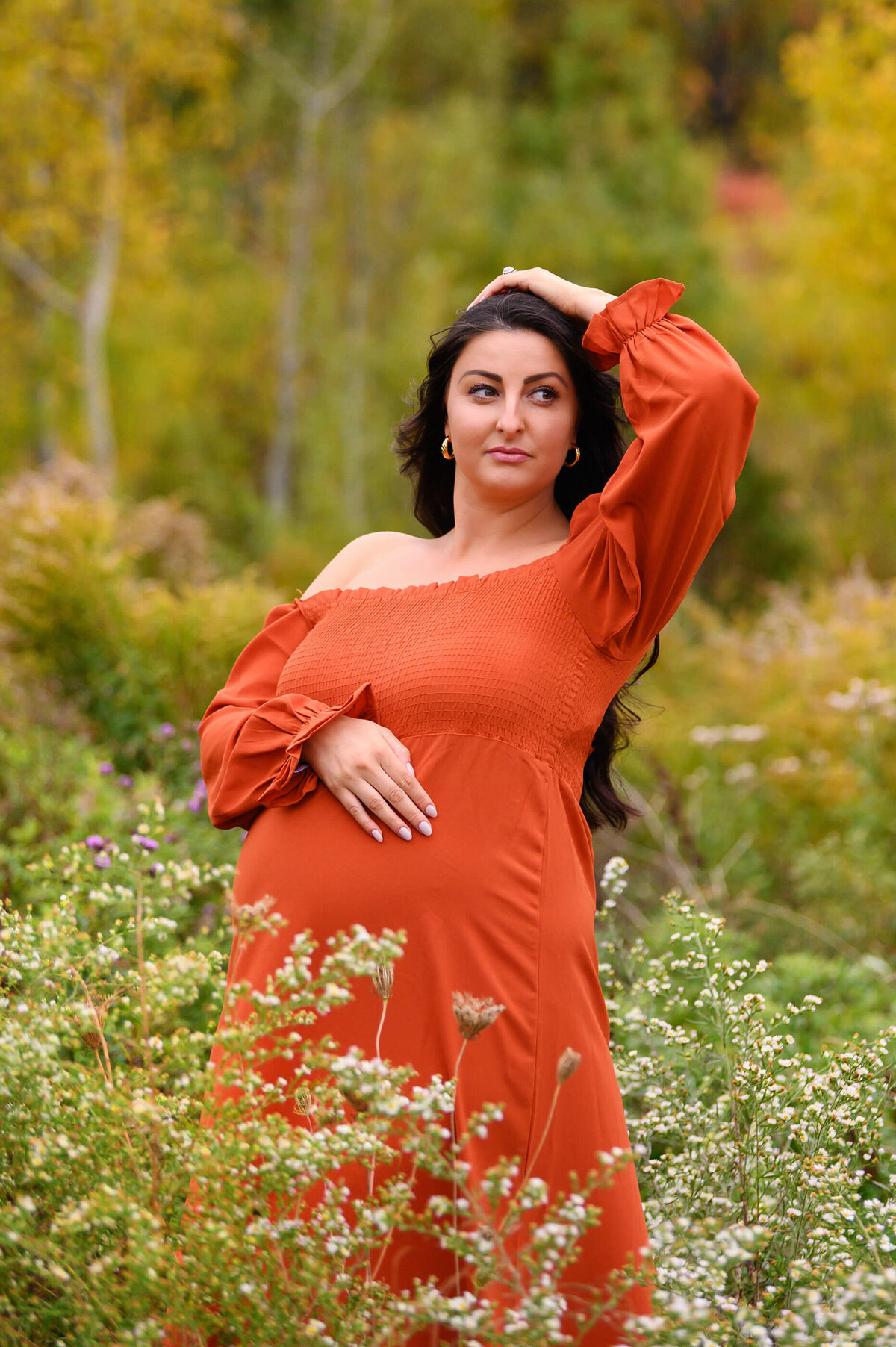 pregnant woman wearing an orange maternity dress with her arm on heard and hand on her belly outdoor maternity photography session in Burlington, On