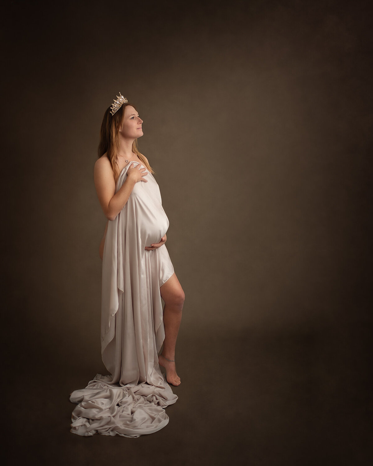 pregnant woman with drapped fabric over belly and crown on at maternity photoshoot