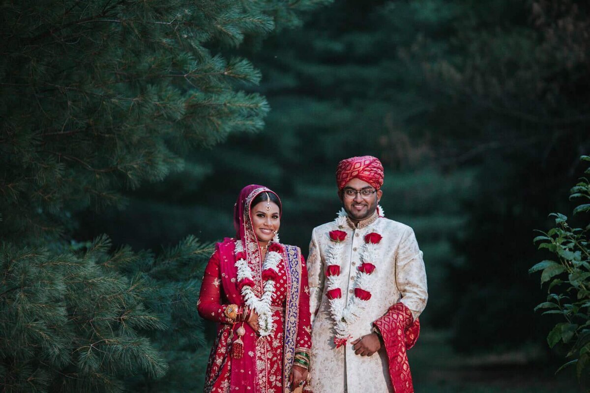 South Asian couple standing side by side surrounded by greenery excited for the day in Philadelphia.