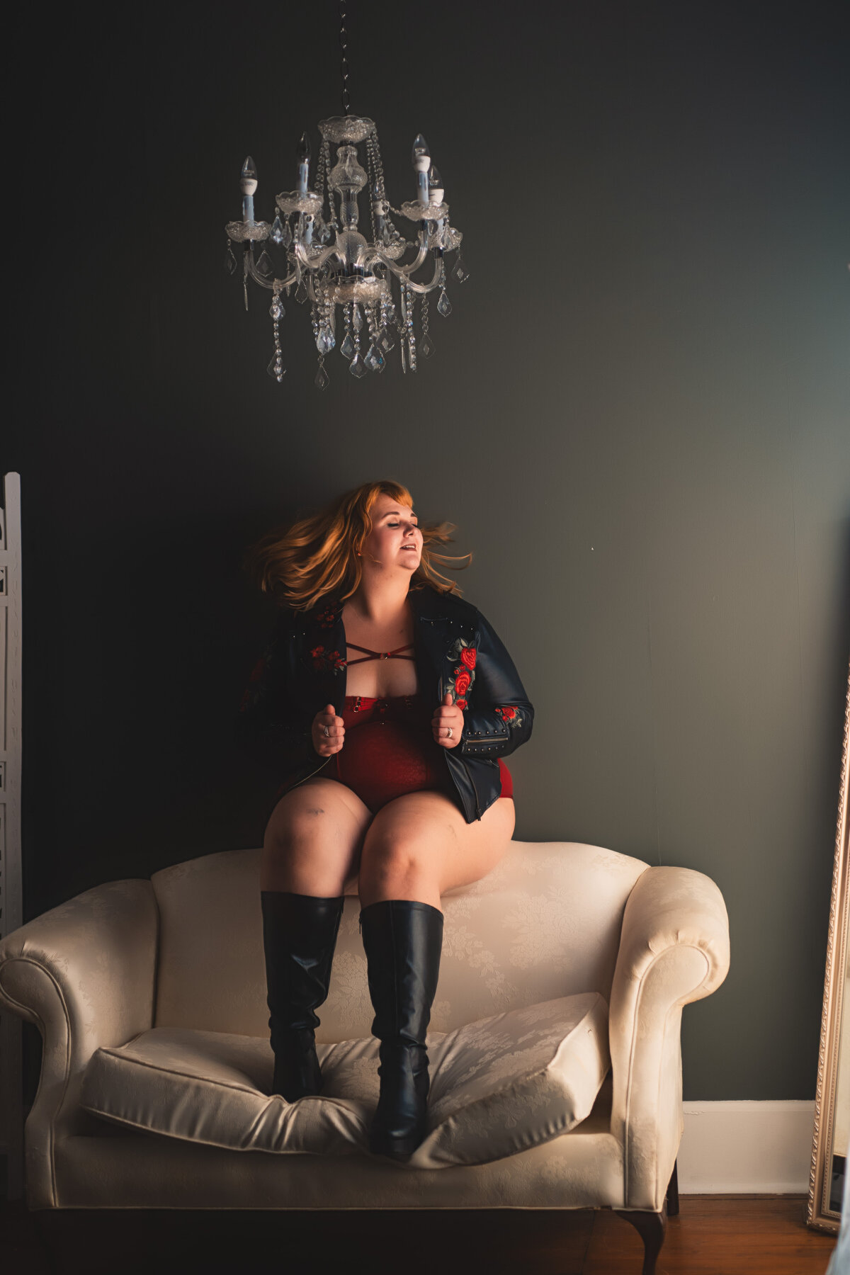 sitting on the back of a couch with a black jacket for her Nashville boudoir photography session