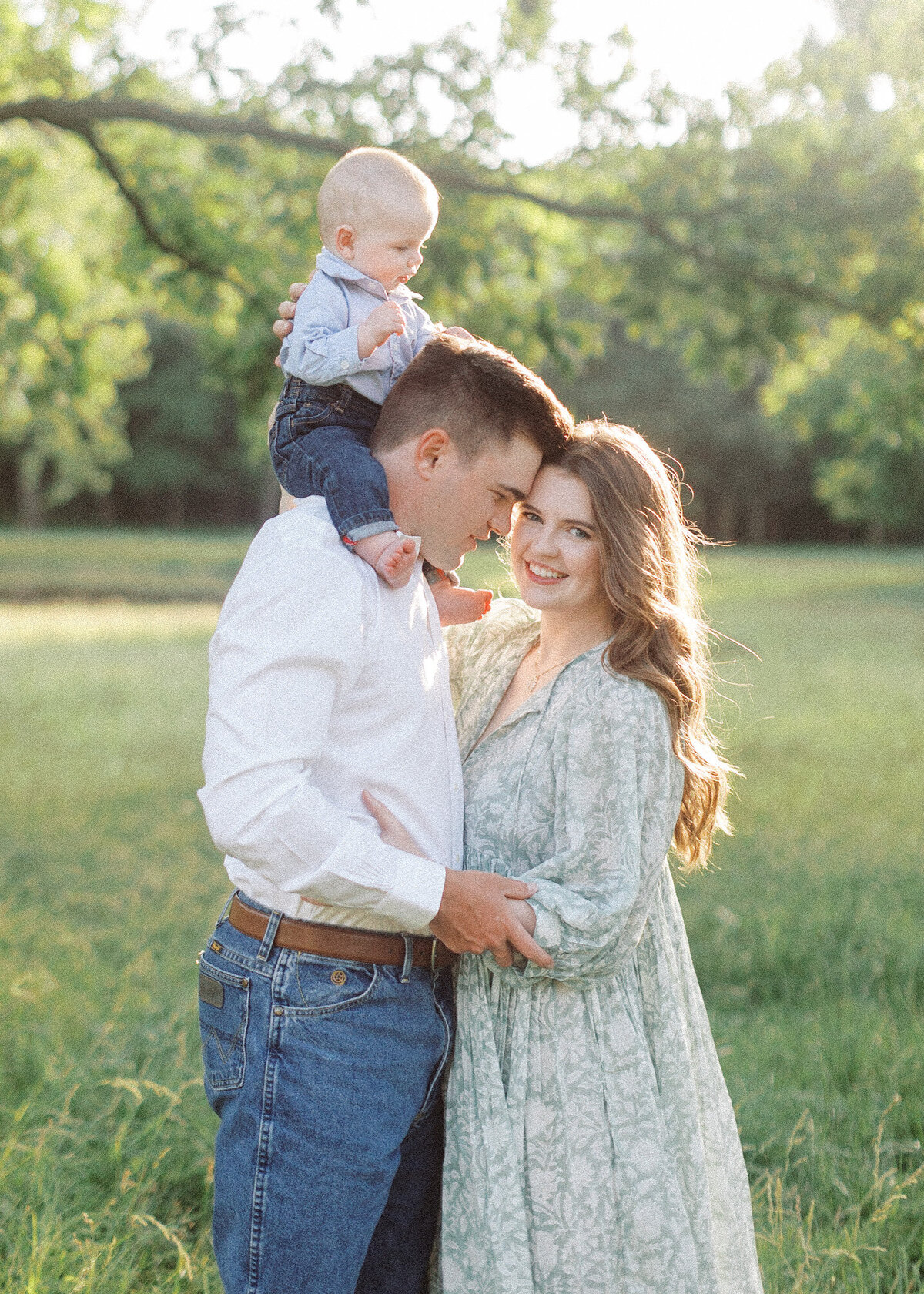 young dad holds young son on shoulders while nuzzling smilling wife