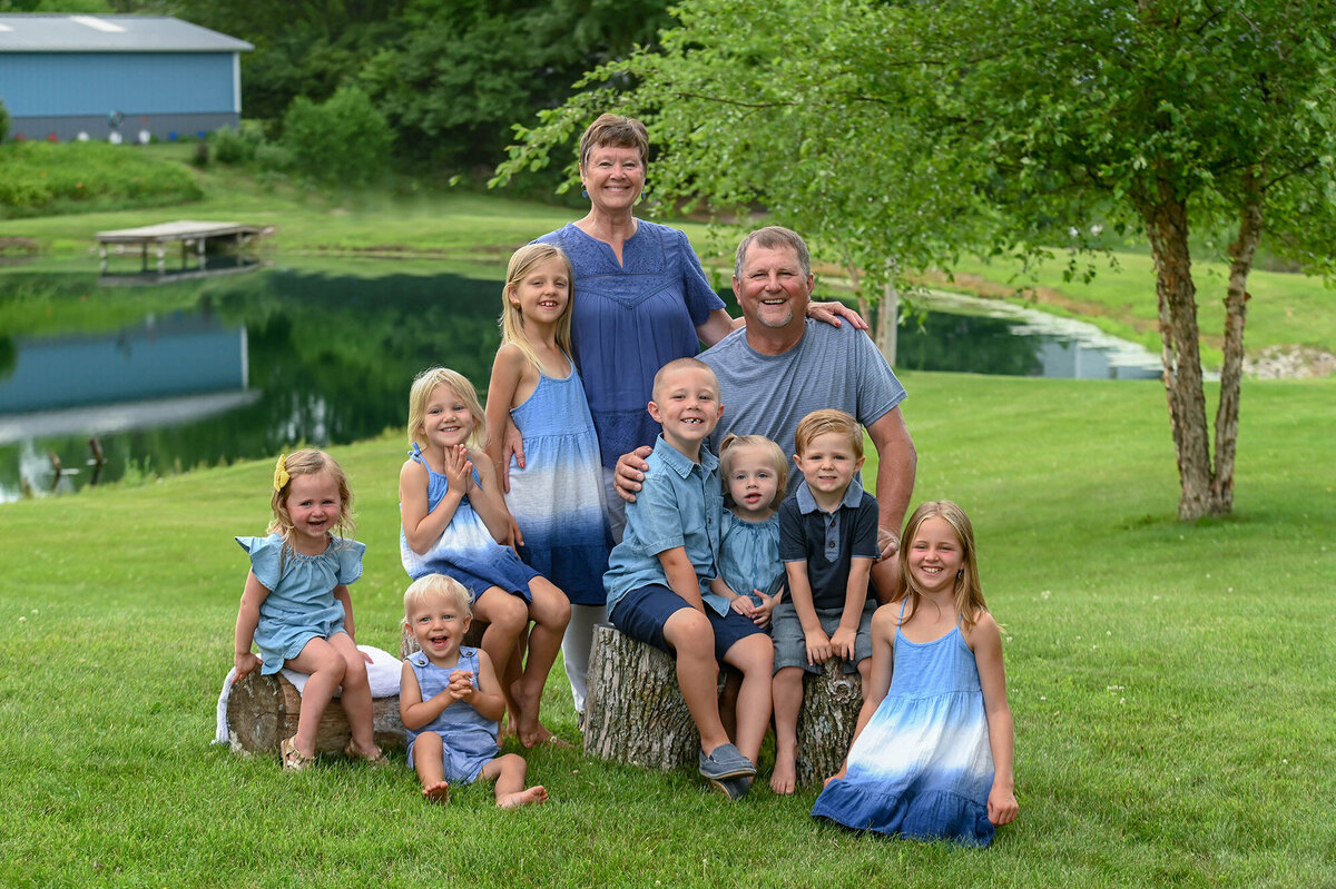 Grandparents and their 8 grandkids sit near a pond for their Iowa Family Photographer