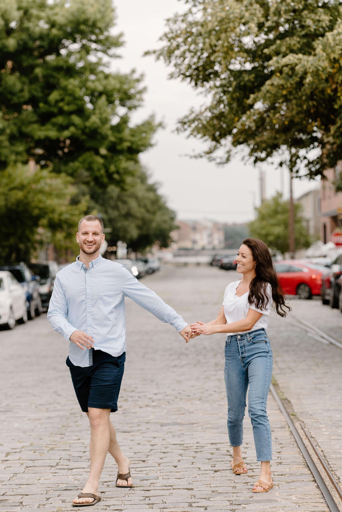 couple holding hands and walking on cobblestone city road in baltimore maryland by sabrina leigh