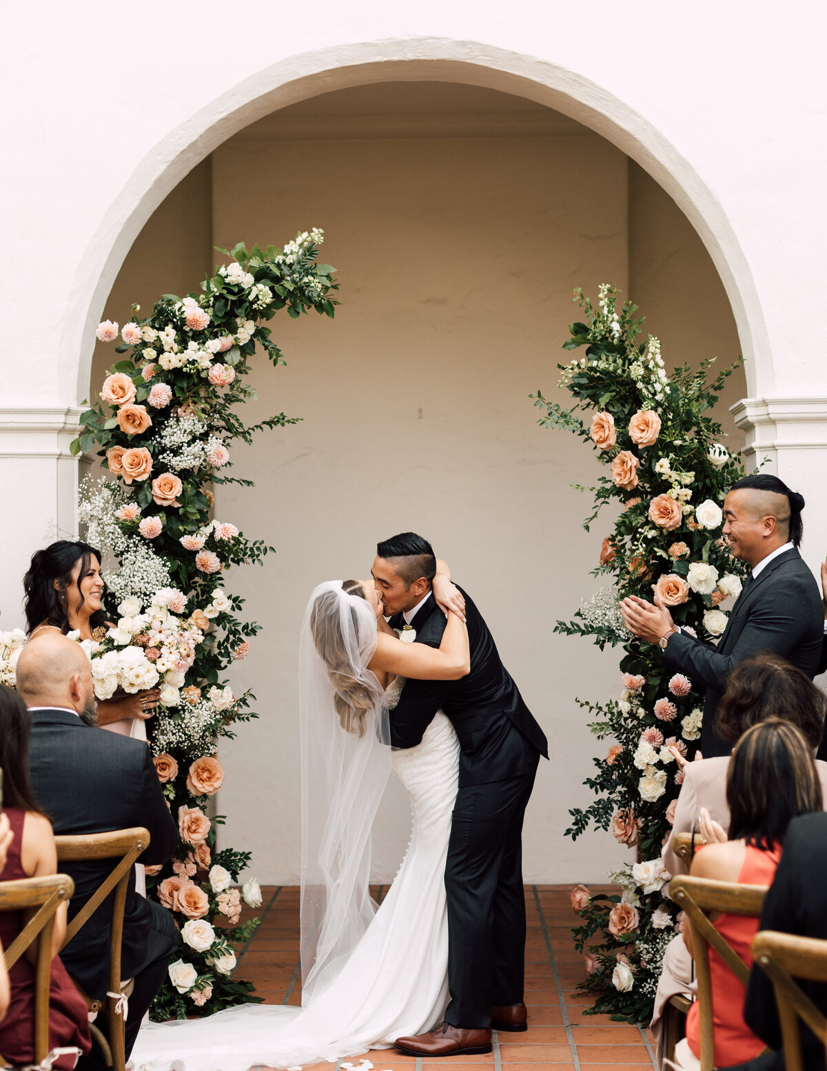 Bride and groom sharing their first kiss at a wedding ceremony surrounded by lush floral arrangements, captured by an Arizona wedding photographer.