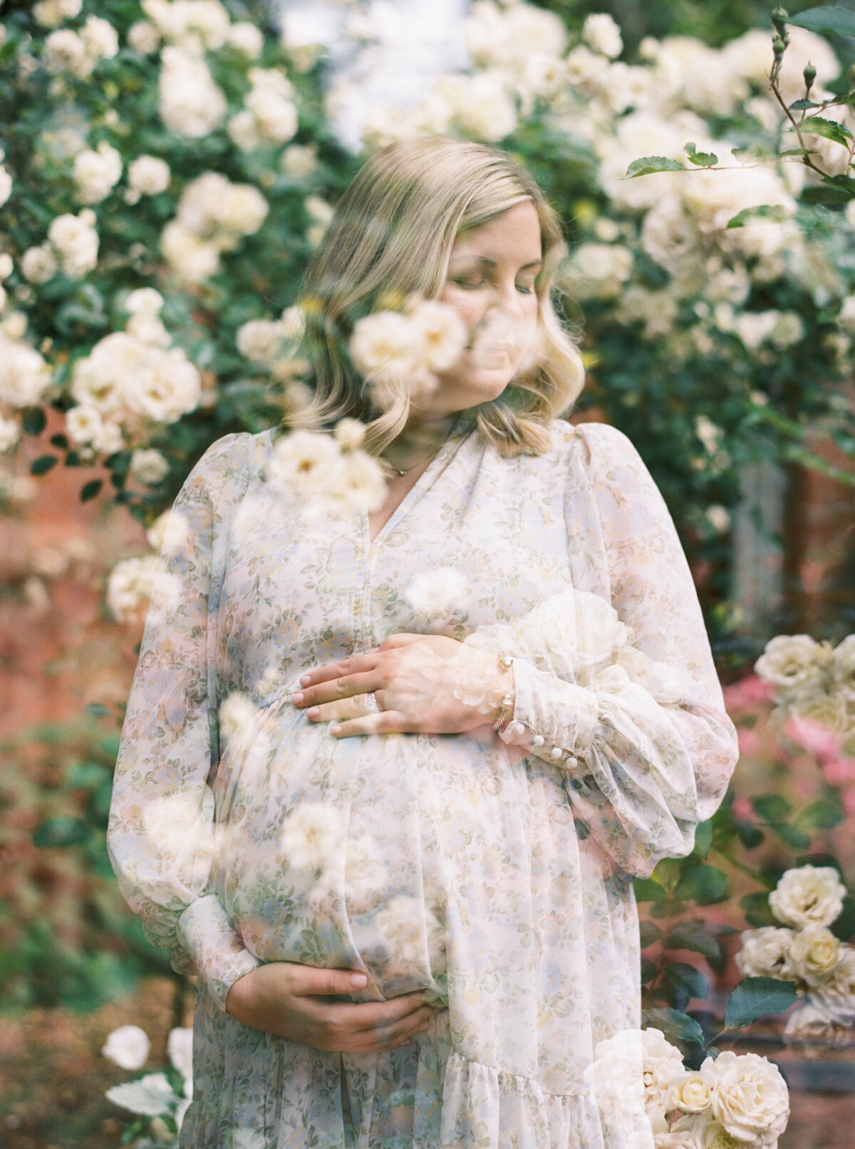 mom holding her pregnant belly in a rose garden. Image by Raleigh maternity photographer A.J. Dunlap Photography.