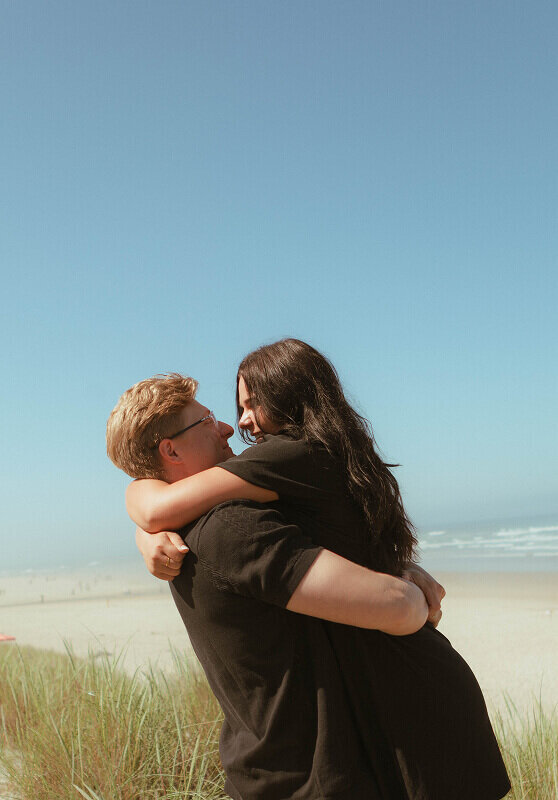 Close up of a man holding his fiancé around the waist and lifting her off the ground. She's holding him around his neck.