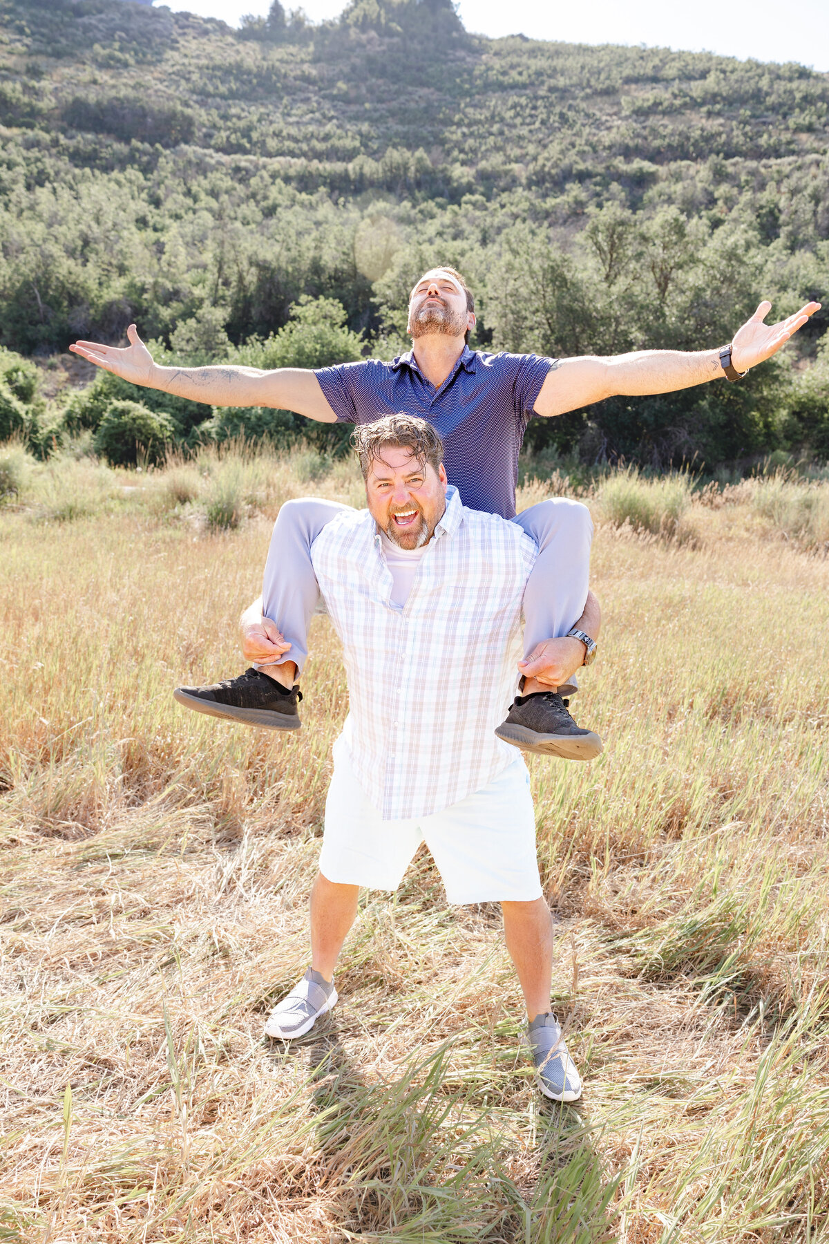 Two brothers sharing a fun and energetic moment, one carrying the other on their shoulders in a bright, golden field.