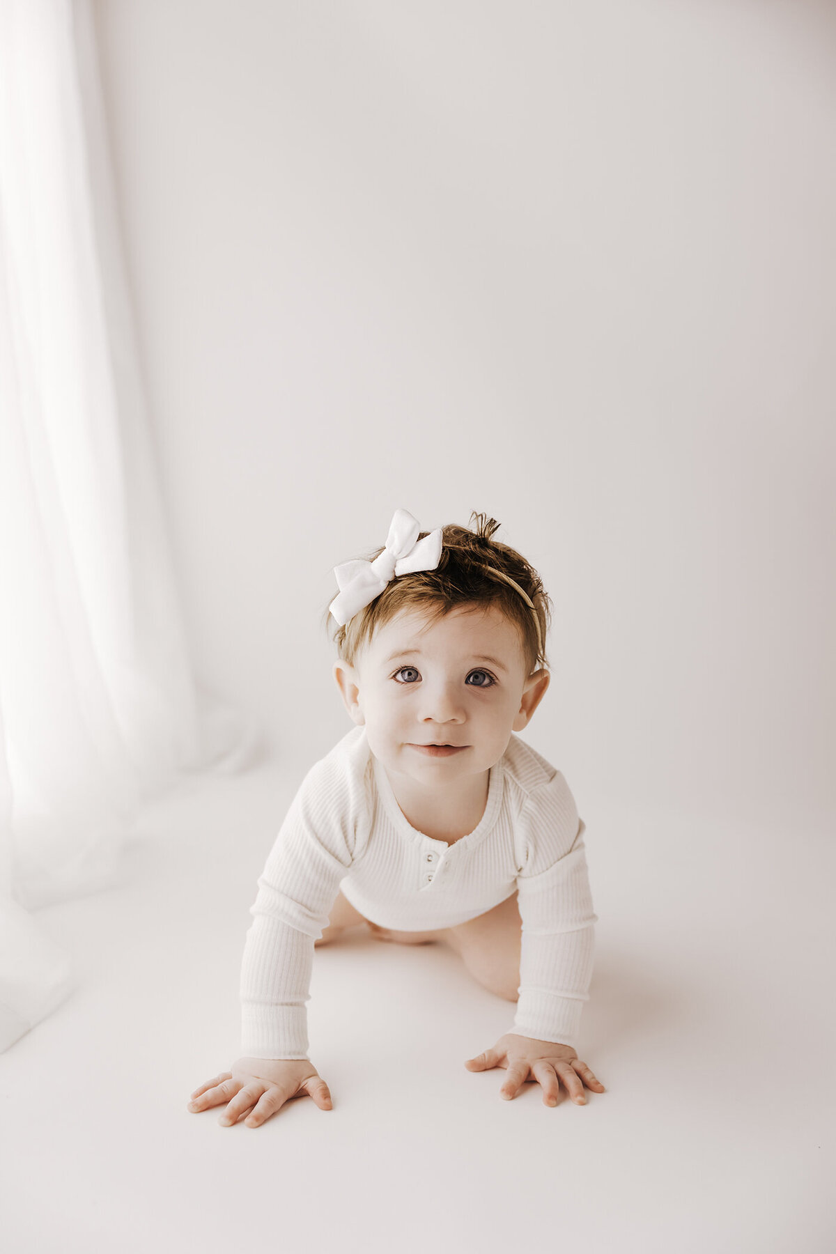 little girl crawling in white outfit on white backdrop
