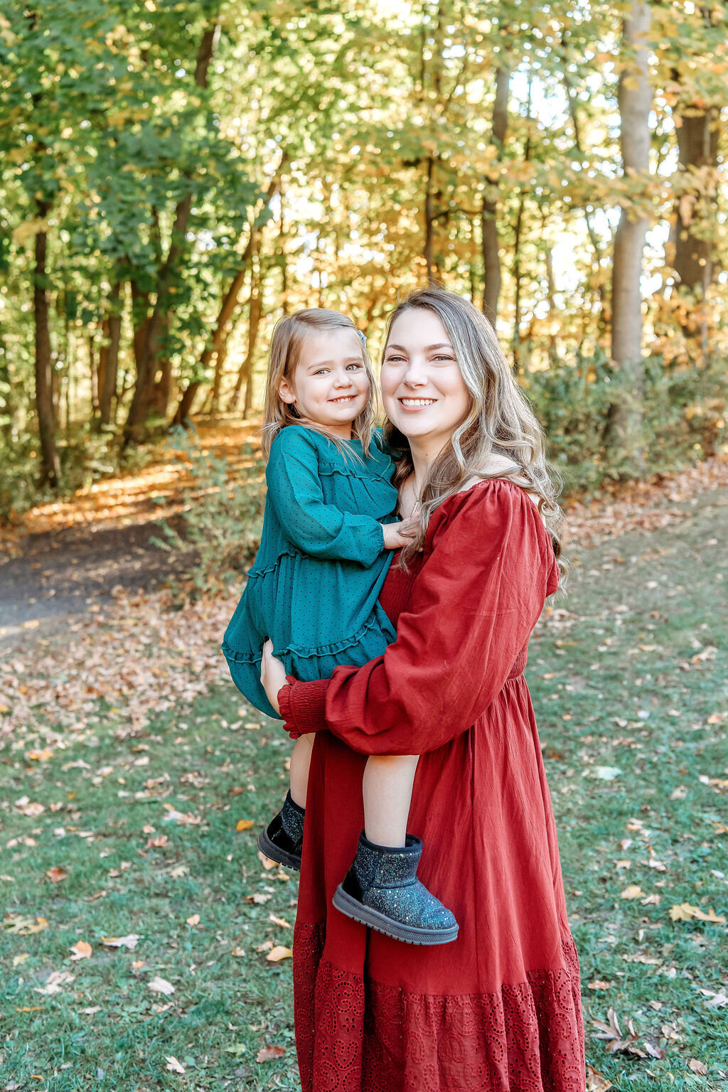 Connecticut family photographer documents mother and daughter bonding moment in matching red and teal outfits among fall trees