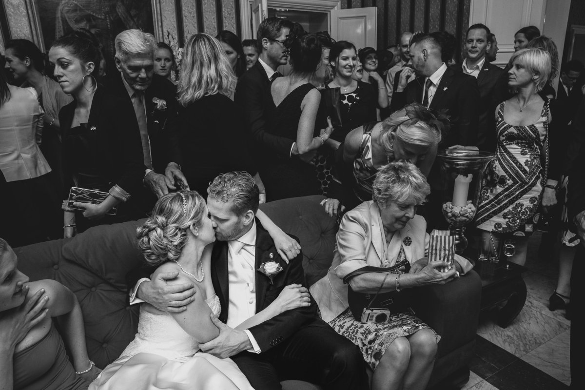 Het bruidspaar verliest zichzelf helemaal in een kus in een zaal vol met mensen. Copyright Nanda Zee-Fritse | FOTOZEE