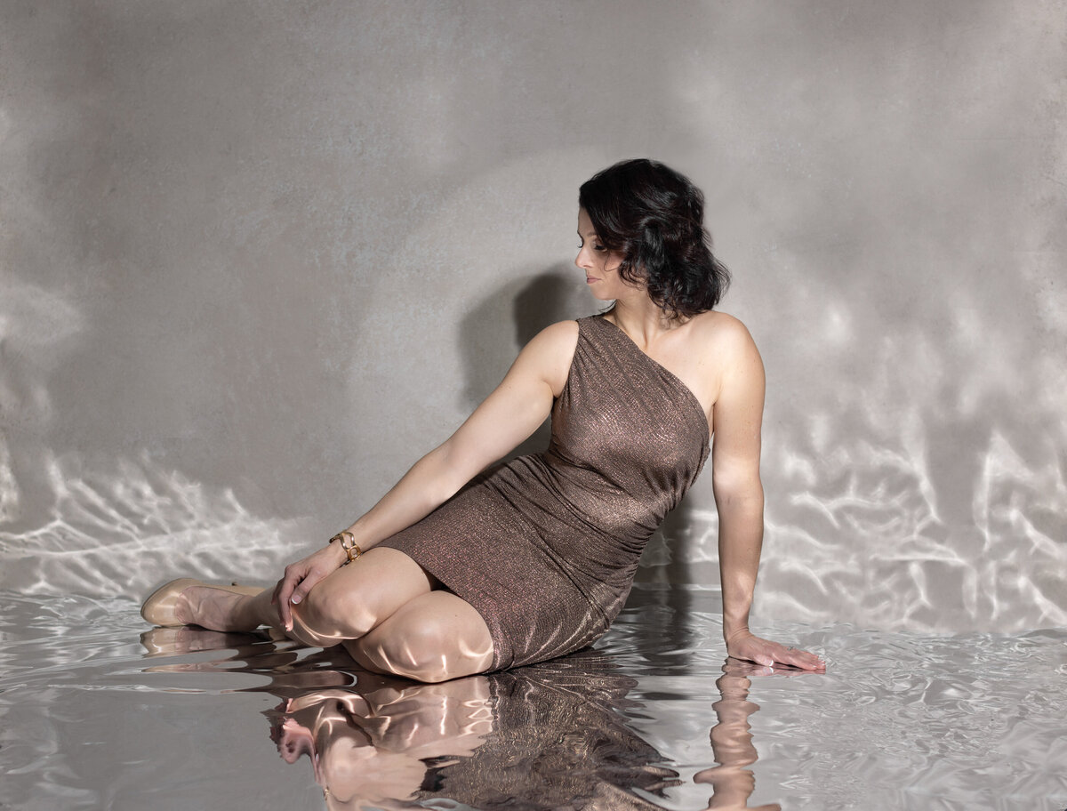 A woman with dark hair and a jewel tone blush dress poses for a portrait as she looks to the side and reclines on what appears to be water in a studio photograph at Janel Lee Photography in Cincinnati Ohio