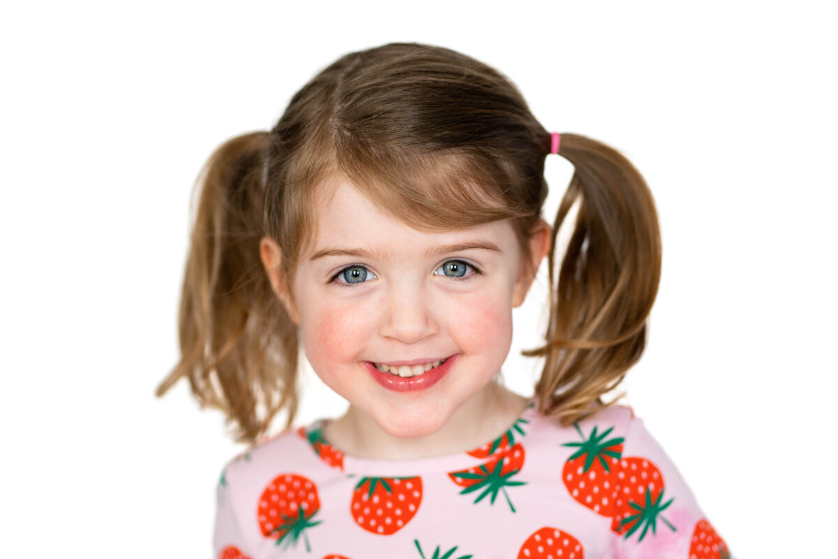 School photo with white background. Little girl wearing strawberry shirt