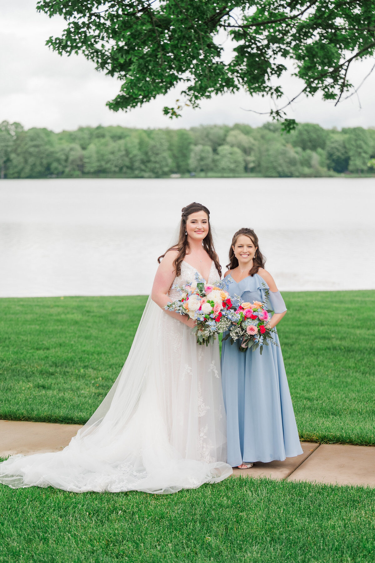 bride and her bridesmaid posing for a wedding picture in front of vineyards at pine lake