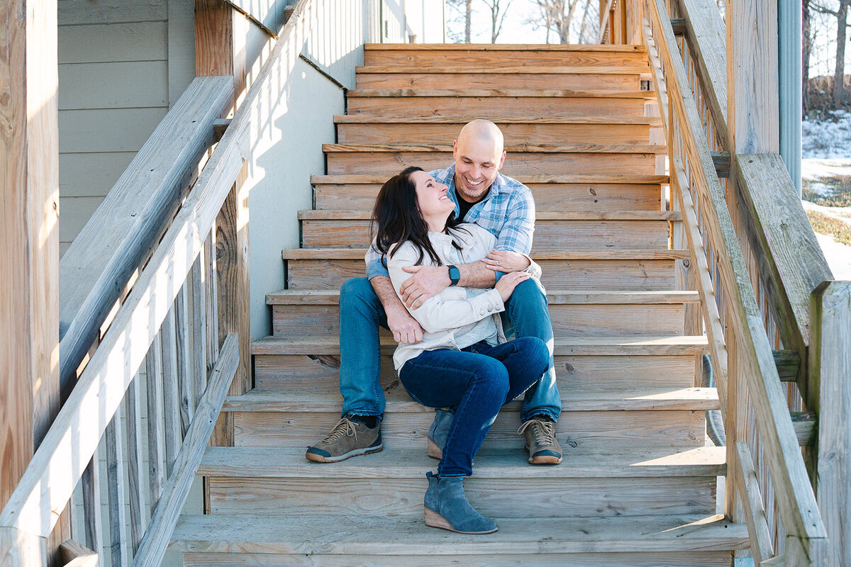 A person sitting on a staircase behind their partner with their arms wrapped around them 